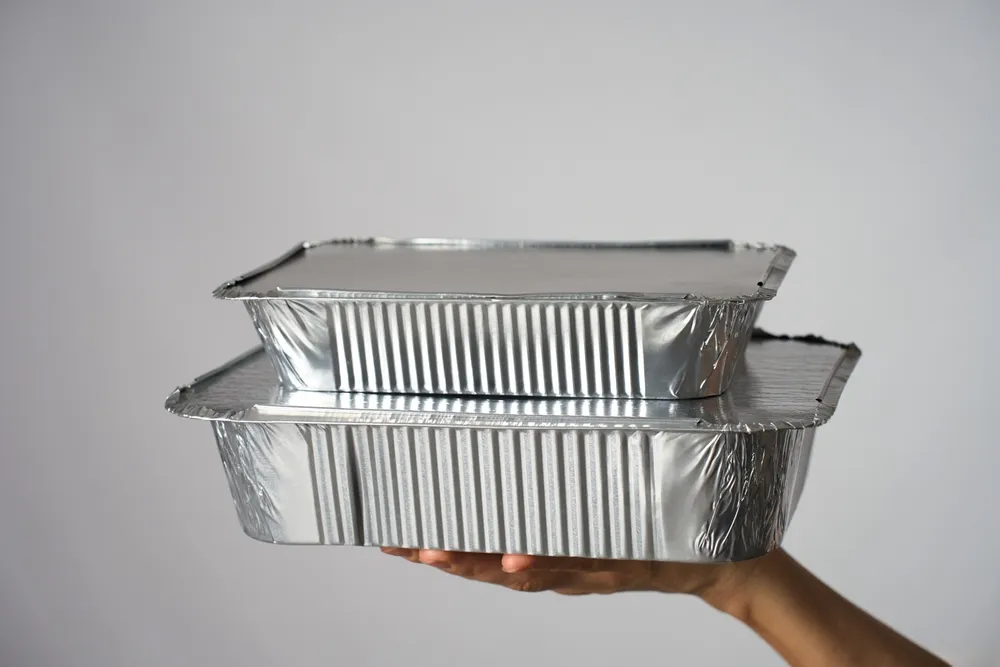 hand holding stack of aluminum covered trays for catering